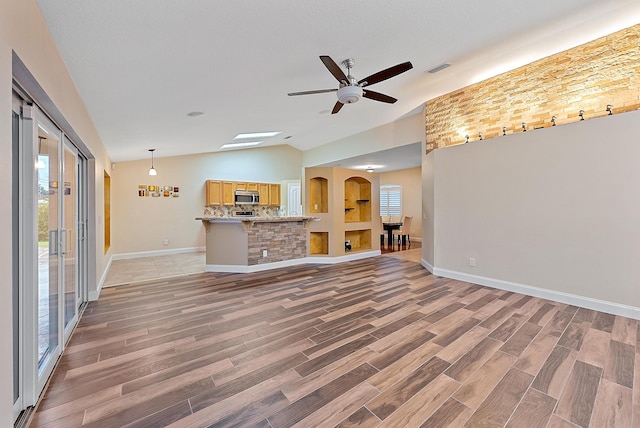 unfurnished living room with light hardwood / wood-style floors, a wealth of natural light, vaulted ceiling, and ceiling fan