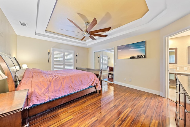 bedroom featuring a tray ceiling, ceiling fan, hardwood / wood-style floors, and ensuite bathroom