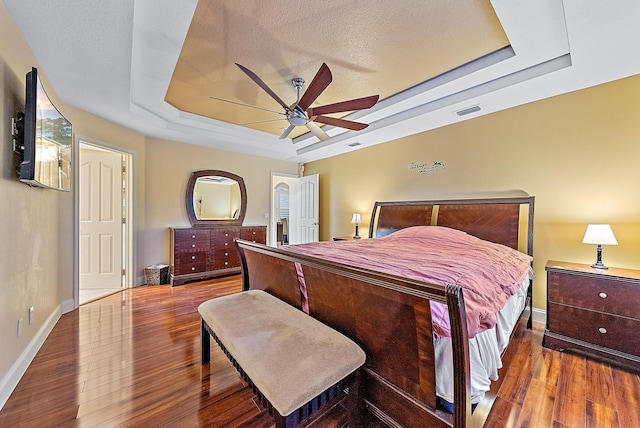 bedroom with a textured ceiling, ceiling fan, a raised ceiling, and hardwood / wood-style flooring