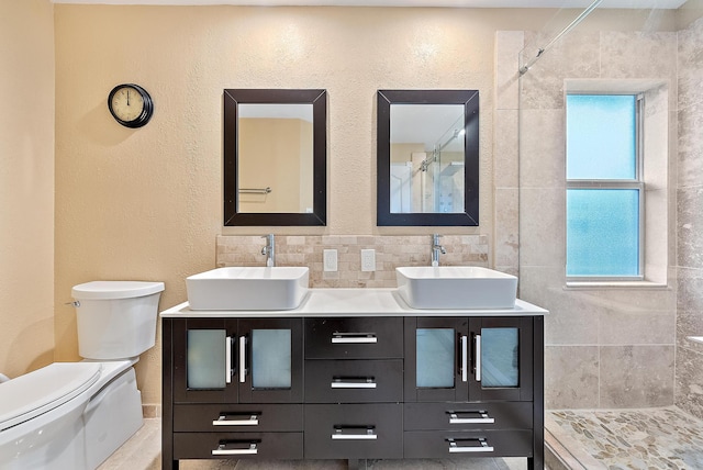 bathroom featuring backsplash, toilet, double vanity, and tile walls