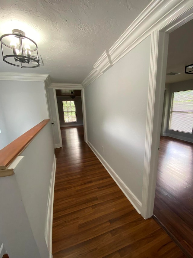 hallway with crown molding, dark hardwood / wood-style flooring, an inviting chandelier, and a textured ceiling