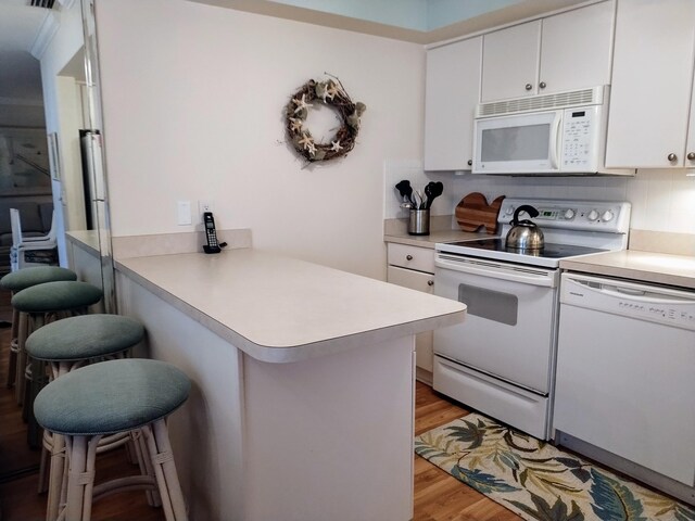 kitchen featuring white appliances, light hardwood / wood-style flooring, kitchen peninsula, and a breakfast bar