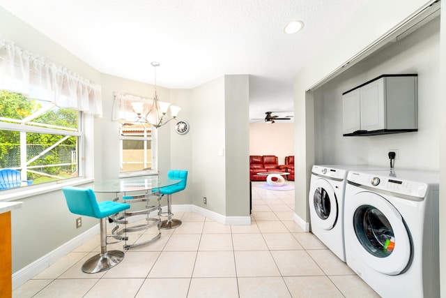 clothes washing area with ceiling fan with notable chandelier, washing machine and dryer, light tile patterned flooring, and cabinets