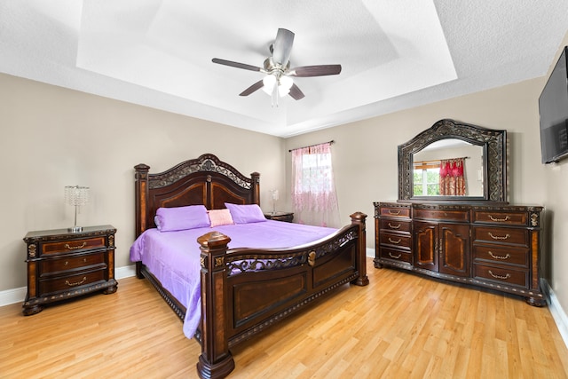 bedroom featuring ceiling fan, a raised ceiling, and light hardwood / wood-style flooring