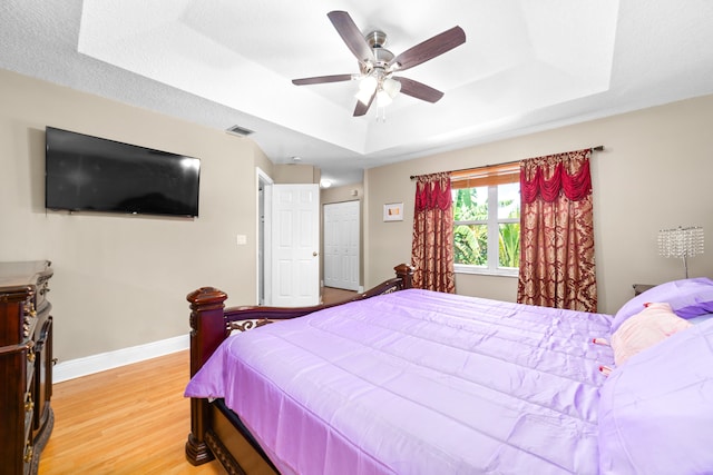 bedroom with ceiling fan, a raised ceiling, and light hardwood / wood-style floors