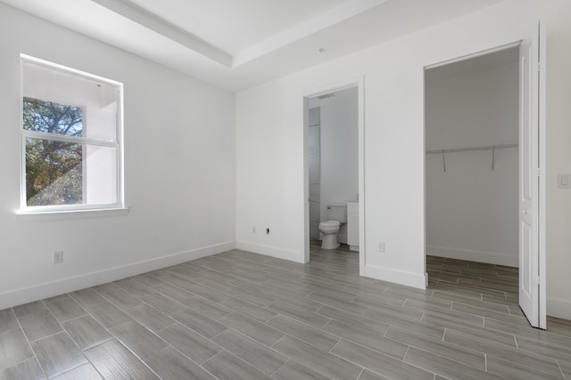 unfurnished bedroom with light wood-type flooring, a walk in closet, and ensuite bath