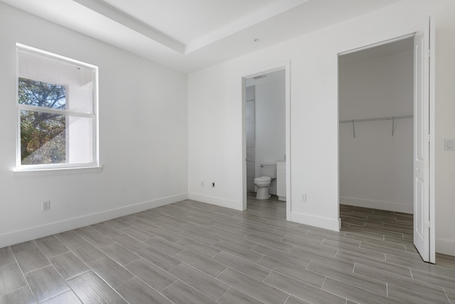 unfurnished bedroom featuring wood finish floors, a walk in closet, ensuite bath, a closet, and baseboards