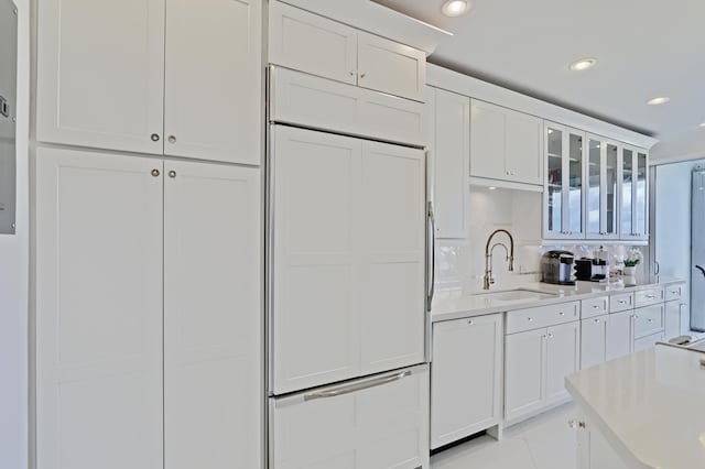 kitchen featuring backsplash, sink, paneled refrigerator, and white cabinets