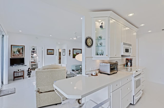 kitchen featuring decorative backsplash, a kitchen bar, white cabinetry, and white appliances