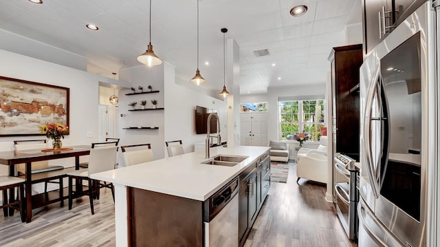 kitchen featuring stainless steel appliances, light hardwood / wood-style floors, sink, a kitchen island with sink, and hanging light fixtures