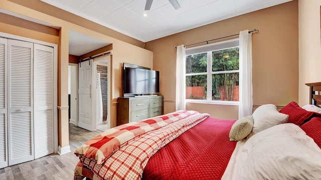 bedroom featuring a closet, ceiling fan, light wood-type flooring, and a barn door