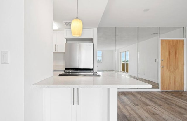 kitchen featuring decorative light fixtures, light stone countertops, light hardwood / wood-style floors, white cabinetry, and stainless steel fridge