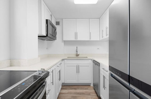 kitchen featuring sink, stainless steel appliances, white cabinetry, and light wood-type flooring