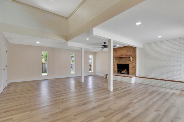 unfurnished living room featuring light hardwood / wood-style floors, ceiling fan, a brick fireplace, and brick wall