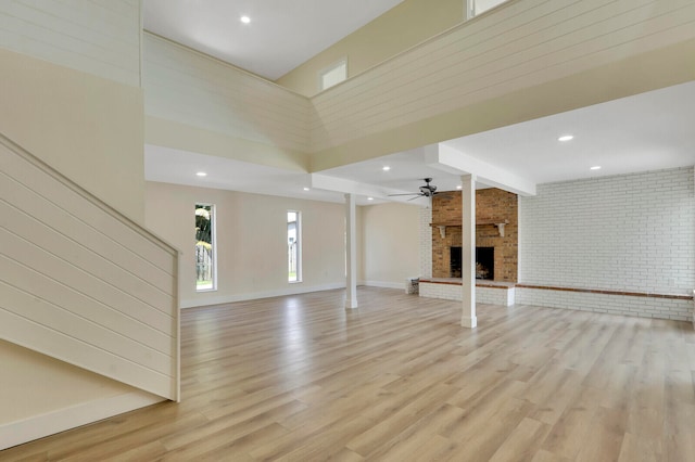 unfurnished living room featuring a towering ceiling, light hardwood / wood-style floors, brick wall, and a fireplace