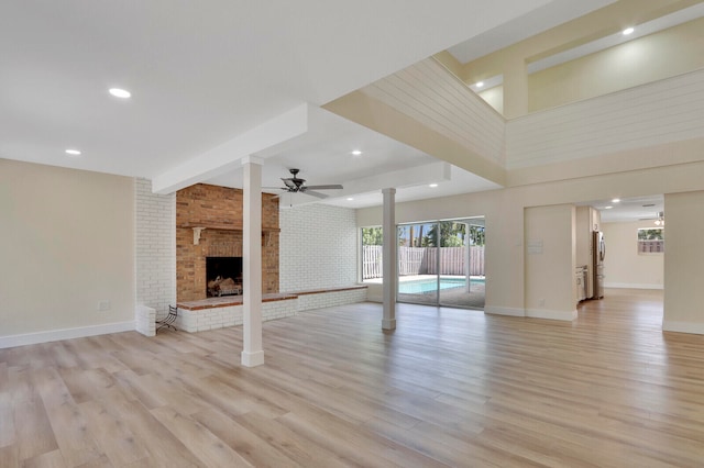 unfurnished living room with ceiling fan, light hardwood / wood-style floors, brick wall, and a fireplace