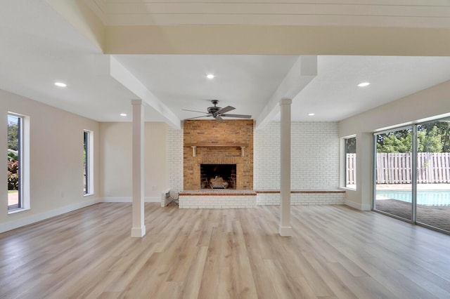 unfurnished living room with light hardwood / wood-style flooring, ceiling fan, a fireplace, and ornate columns