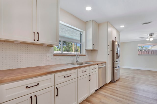 kitchen with appliances with stainless steel finishes, light hardwood / wood-style floors, white cabinetry, butcher block counters, and sink