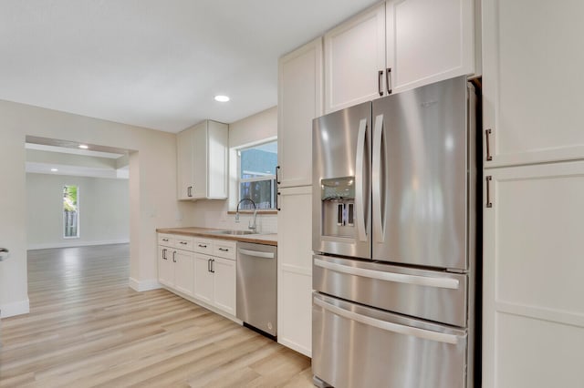 kitchen with sink, backsplash, white cabinetry, stainless steel appliances, and light wood-type flooring