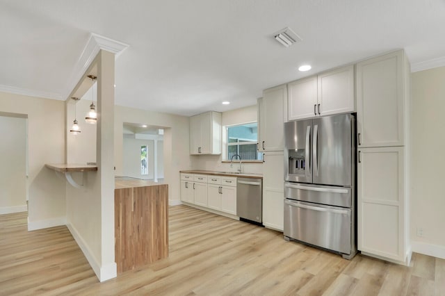 kitchen featuring light wood-type flooring, hanging light fixtures, stainless steel appliances, and white cabinets