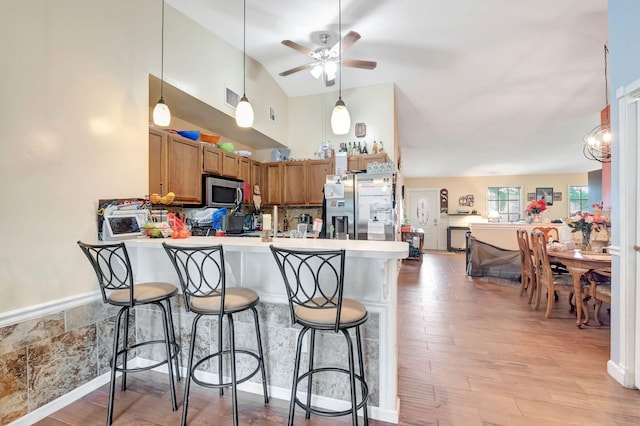 kitchen with a peninsula, a breakfast bar, light countertops, appliances with stainless steel finishes, and brown cabinets