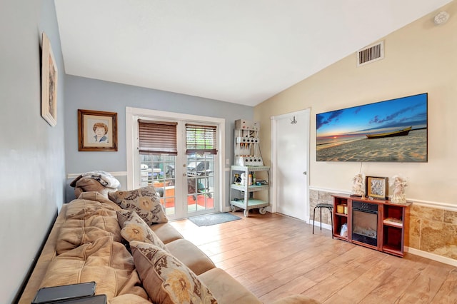 living area featuring vaulted ceiling, light wood-style flooring, a fireplace, and visible vents