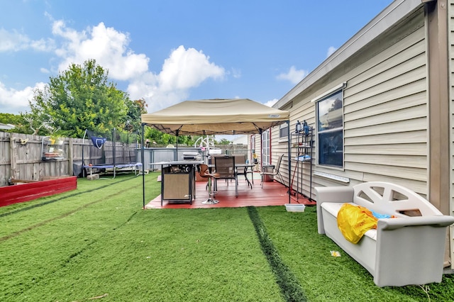 view of yard featuring a gazebo, a trampoline, a fenced backyard, and a wooden deck