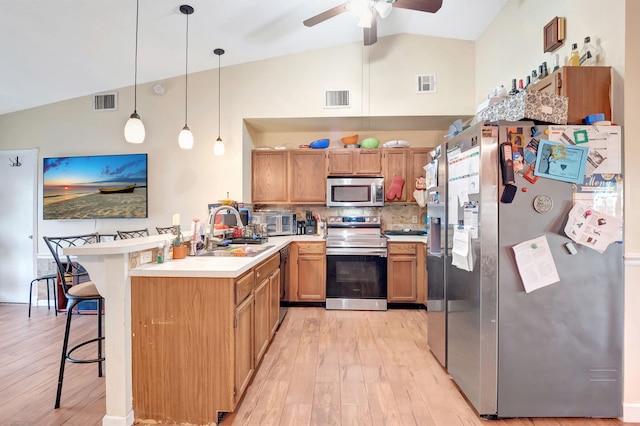 kitchen featuring decorative light fixtures, stainless steel appliances, light countertops, visible vents, and a kitchen bar