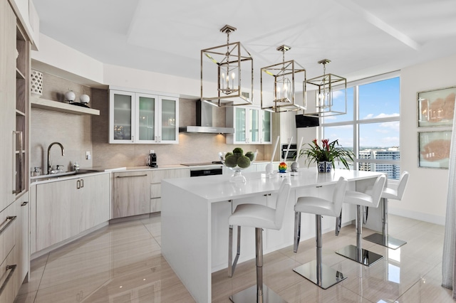 kitchen featuring a kitchen island with sink, wall chimney exhaust hood, hanging light fixtures, backsplash, and a kitchen bar