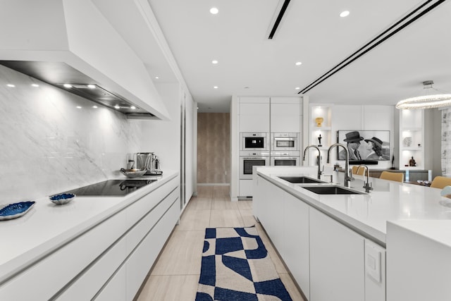 kitchen with black electric stovetop, custom exhaust hood, multiple ovens, sink, and white cabinets