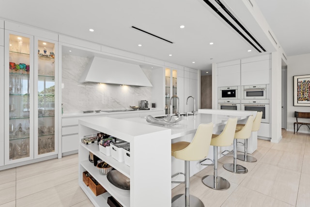 kitchen with a large island, a breakfast bar, white cabinets, and custom exhaust hood