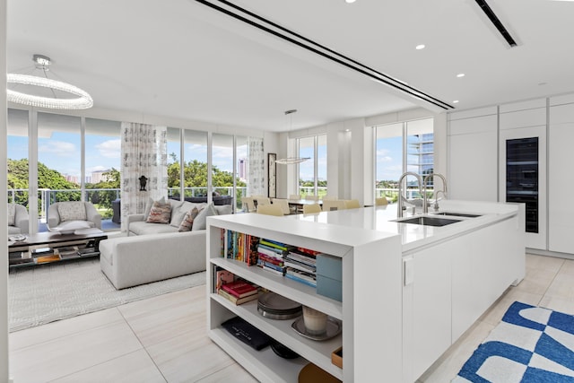 kitchen with a wealth of natural light, sink, light tile patterned floors, an island with sink, and white cabinets