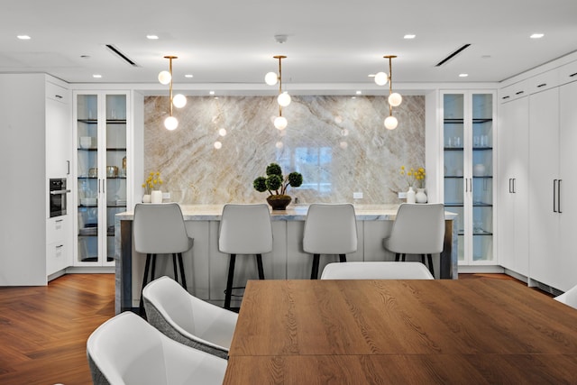 kitchen with dark parquet flooring, white cabinetry, wall oven, light stone counters, and pendant lighting