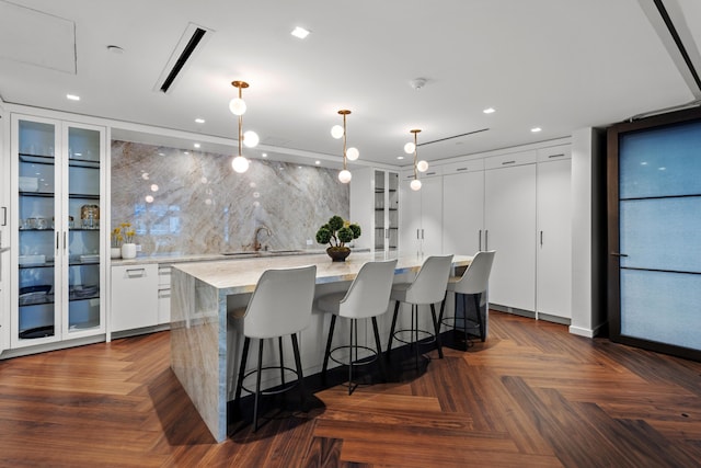 kitchen featuring dark parquet flooring, a large island, hanging light fixtures, decorative backsplash, and white cabinets