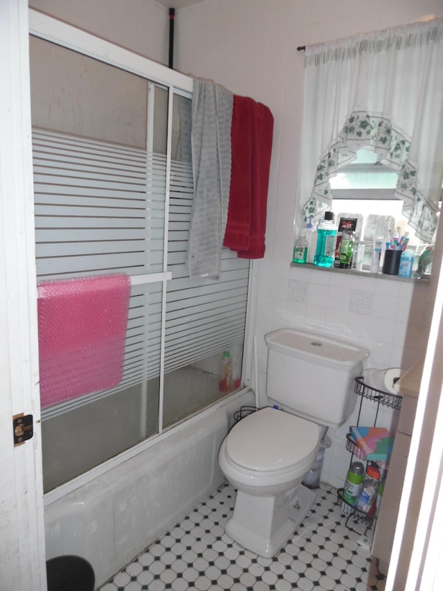 bathroom featuring combined bath / shower with glass door, tile patterned floors, tile walls, and toilet