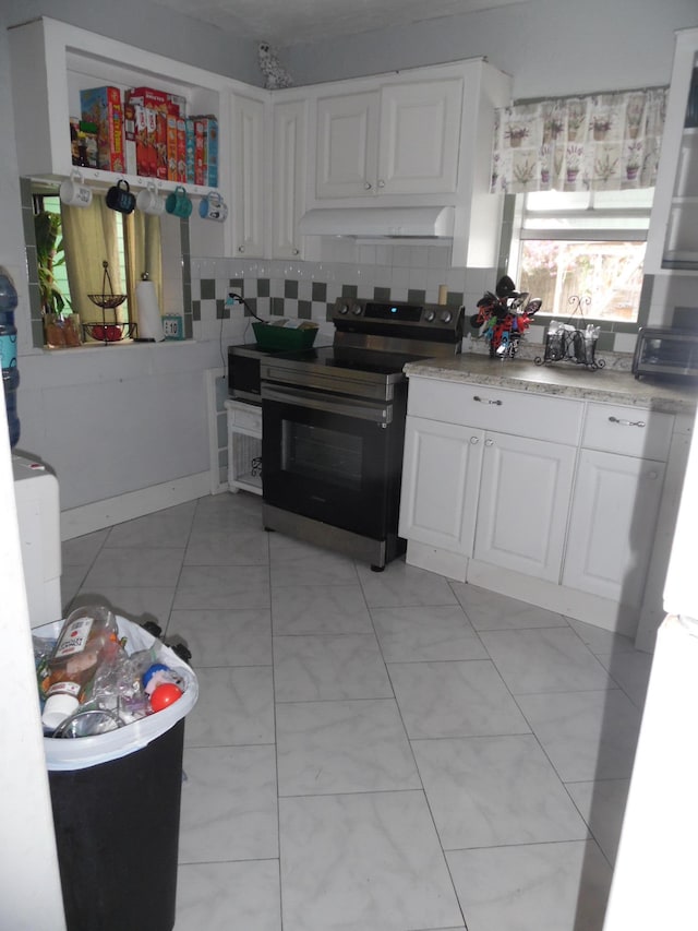 kitchen featuring black range with electric stovetop, backsplash, light tile patterned floors, and white cabinets