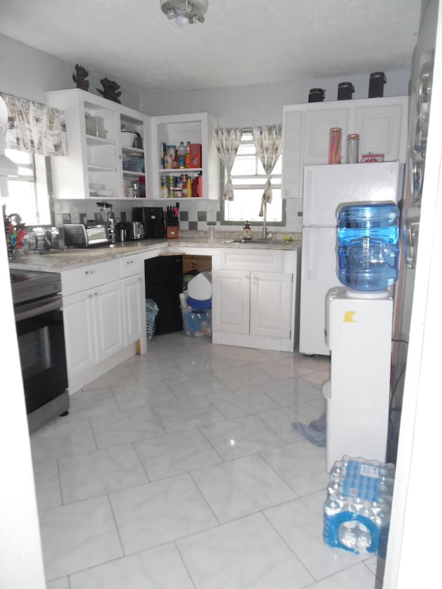 kitchen featuring range, light tile patterned floors, fridge, and white cabinetry