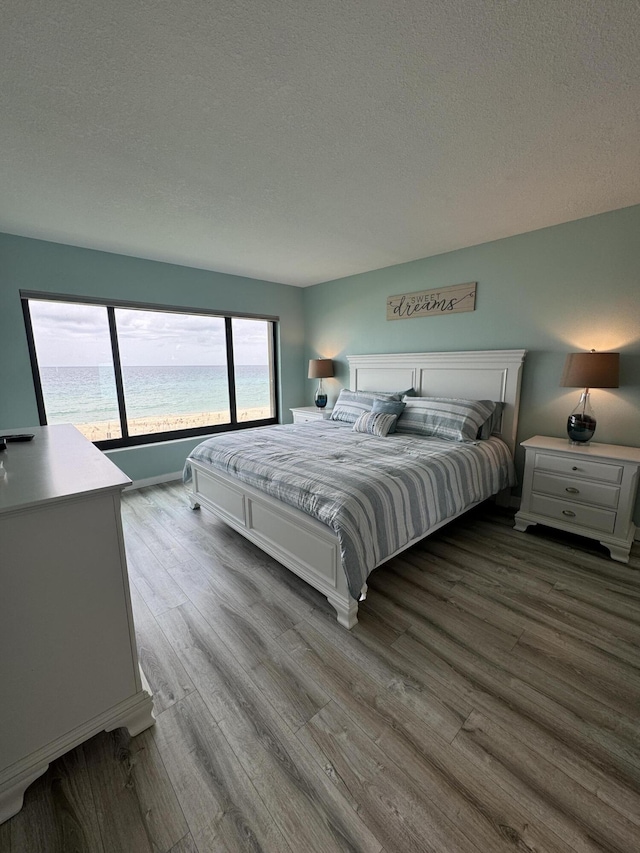 bedroom with a textured ceiling, a water view, and light hardwood / wood-style floors