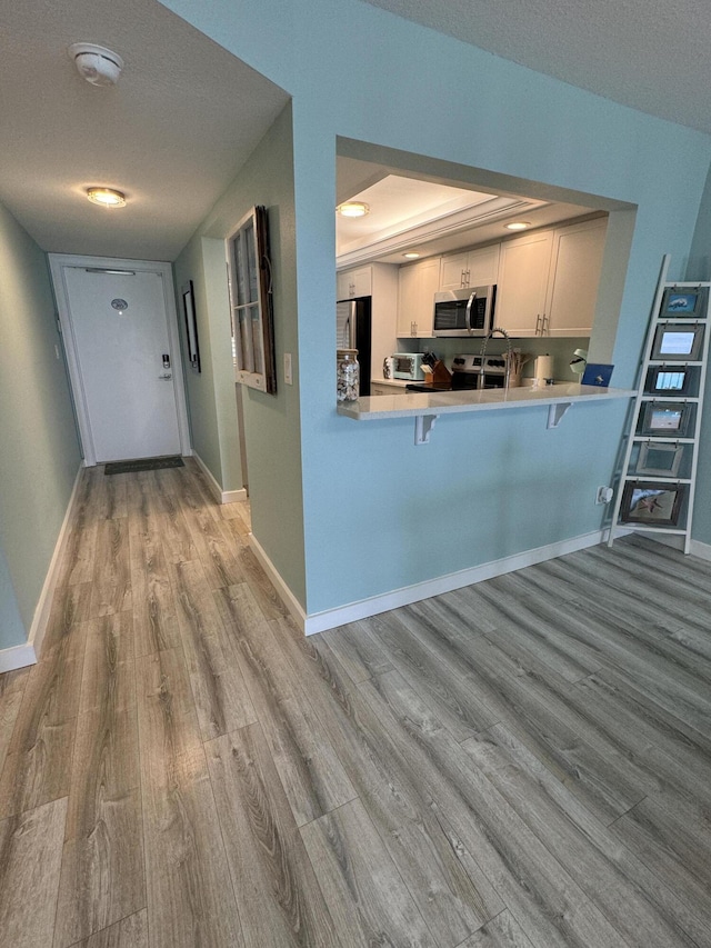 kitchen featuring white cabinetry, stainless steel appliances, light hardwood / wood-style flooring, kitchen peninsula, and a breakfast bar