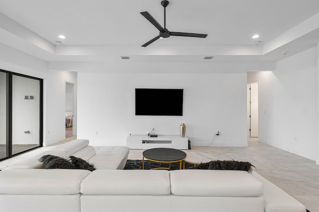 living room featuring a tray ceiling, ceiling fan, and light tile patterned flooring