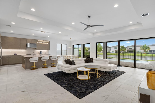 tiled living room featuring ceiling fan, a raised ceiling, and sink