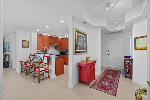 kitchen featuring visible vents, dark countertops, a breakfast bar, brown cabinets, and under cabinet range hood