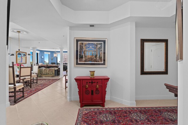 hallway with light tile patterned floors, a tray ceiling, and ornate columns