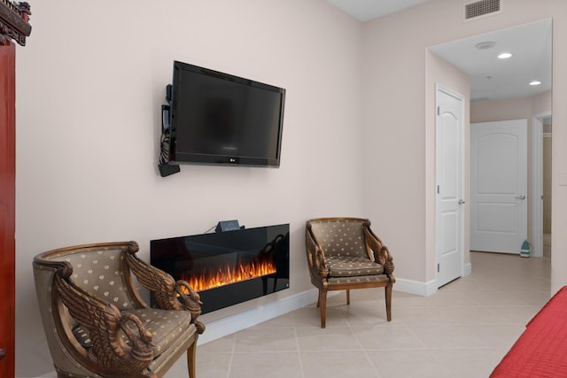 living area featuring a warm lit fireplace, tile patterned flooring, visible vents, and baseboards