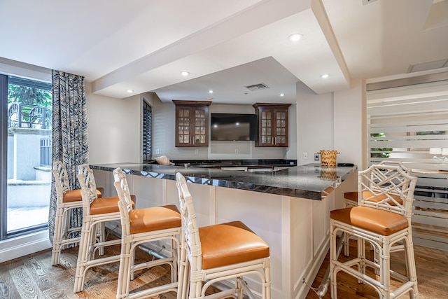 kitchen featuring hardwood / wood-style flooring, kitchen peninsula, a kitchen breakfast bar, and dark brown cabinetry