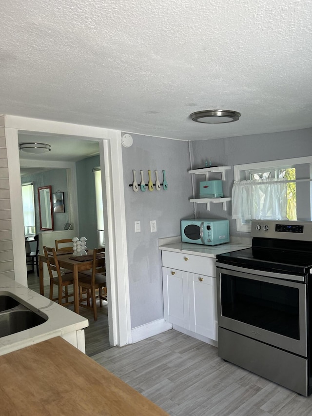 kitchen featuring a textured ceiling, white cabinets, light hardwood / wood-style floors, and stainless steel range with electric stovetop