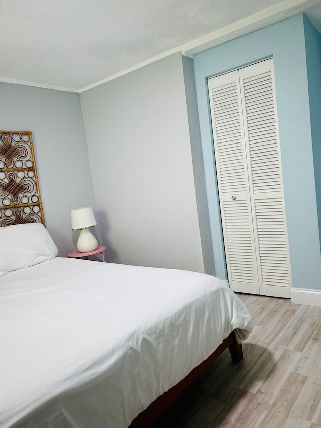 bedroom featuring crown molding, a closet, light hardwood / wood-style floors, and a textured ceiling