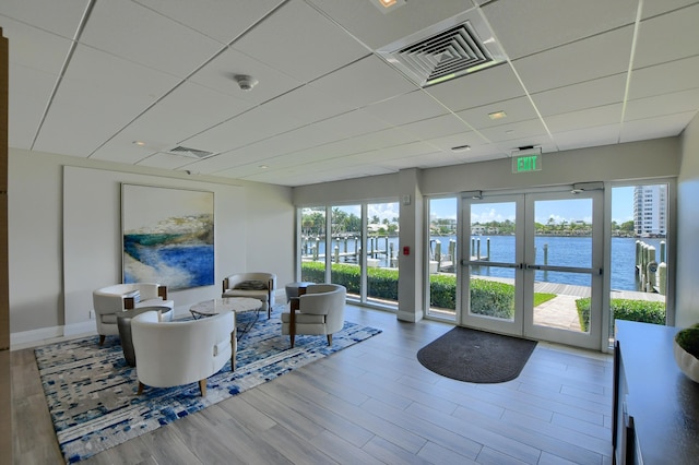 living room with a drop ceiling, light hardwood / wood-style floors, a water view, and french doors