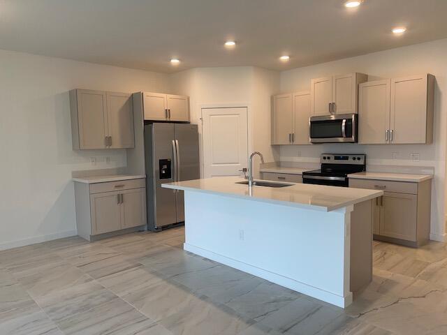 kitchen with stainless steel appliances, sink, gray cabinetry, a kitchen island with sink, and light tile patterned floors