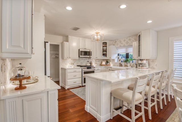 kitchen featuring white cabinets, decorative backsplash, dark hardwood / wood-style flooring, kitchen peninsula, and stainless steel appliances